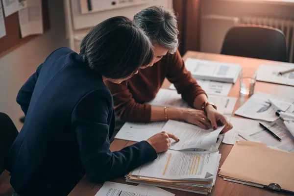 Illustration: two people at a table reviewing documents, seen from behind.