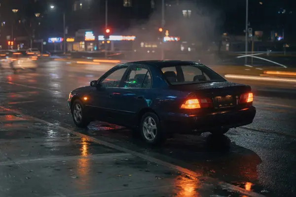 Illustration: a car waiting at a city kerb at night.